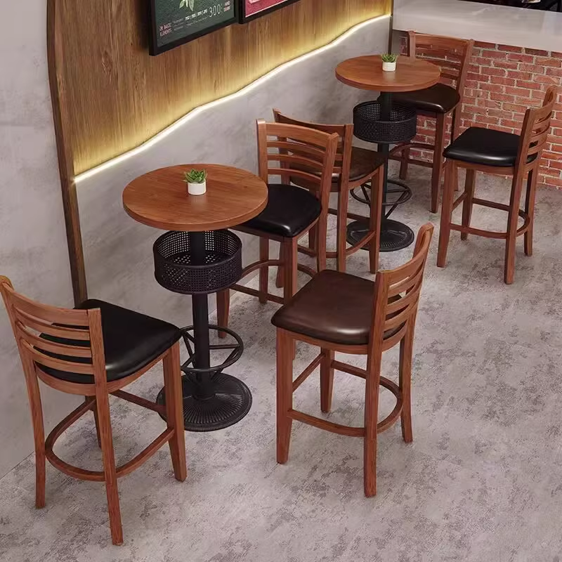 Wooden bar stools with black leather cushions and small round tables, placed in a modern bar setting.