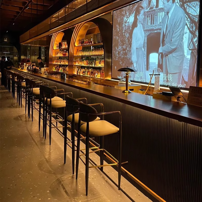 Premium seating at a modern bar counter, illuminated with a cozy ambiance and sleek designs, highlighting comfortable stools and a long bar counter.