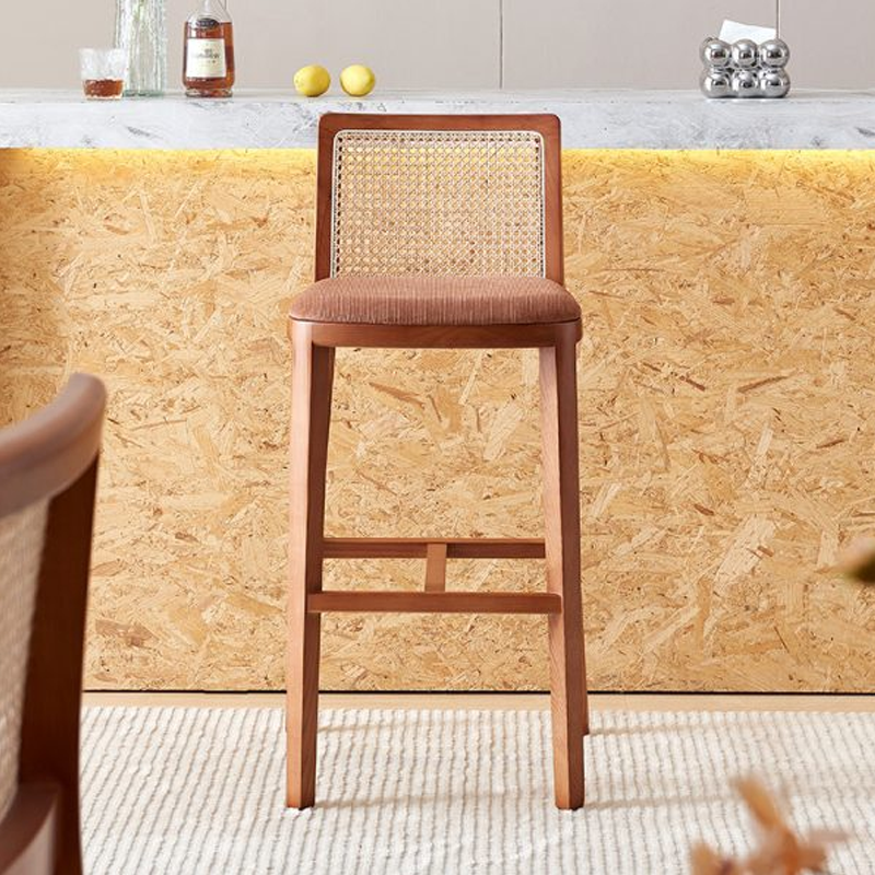 A high-back wooden bar stool with a rattan backrest and cushioned seating, set against a warm-toned bar counter.