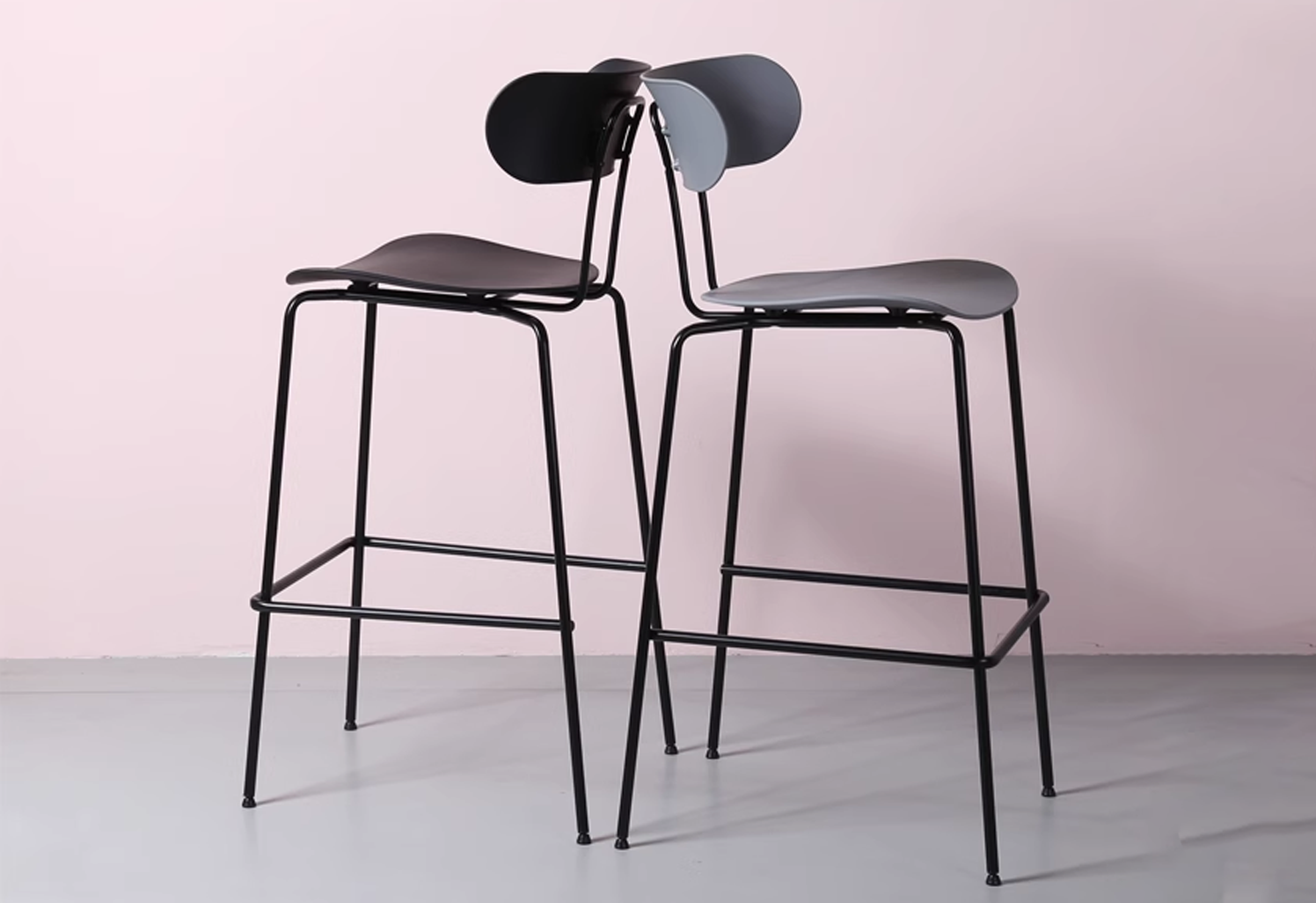 A pair of minimalist bar stools with black metal frames and matte-finish seats in black and grey, arranged in a modern interior.