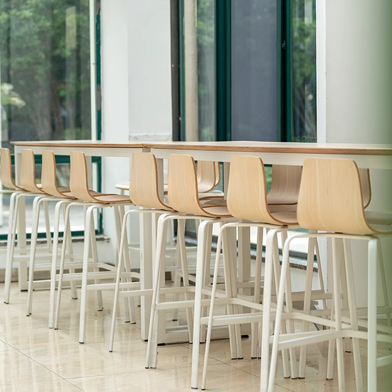 minimalist white and wooden bar stools at a modern dining table, with clean lines and large windows in the background.