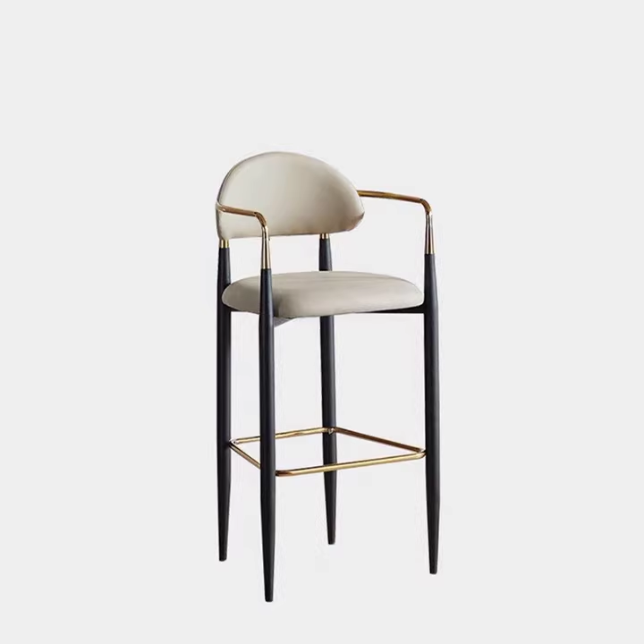 A stylish bar stool with black metal frame and gold accents, featuring a comfortable backrest and seat in light beige.