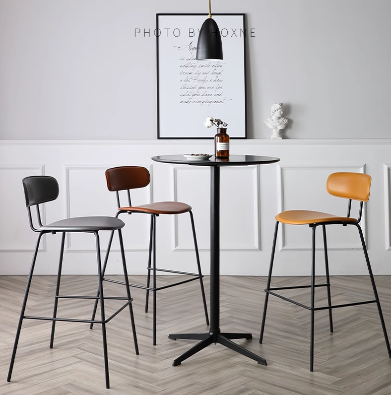 A set of three modern bar stools in black, brown, and mustard yellow with a sleek round black table, arranged in a contemporary interior setting.