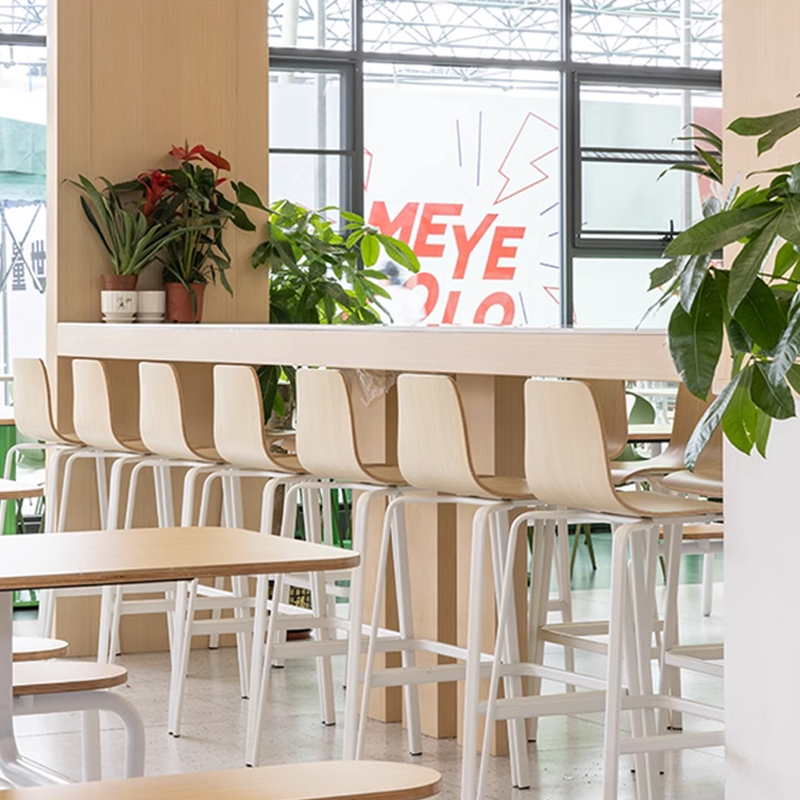 modern white and wood bar stools at a stylish coffee shop counter, with plants and large windows visible.