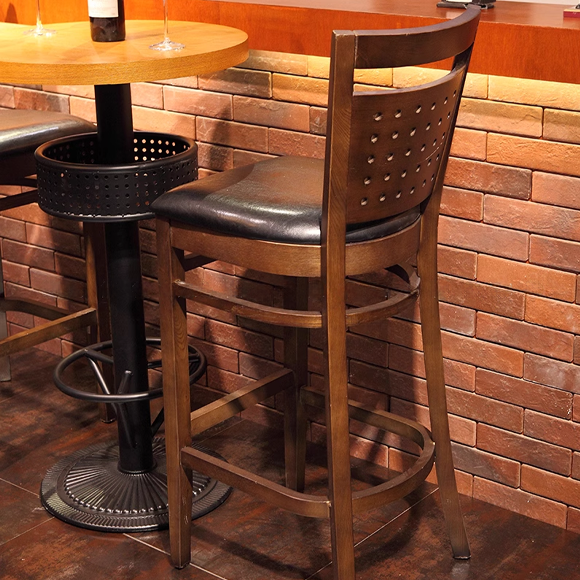 Wooden barstool with perforated back and black cushioned seat at a bar table.