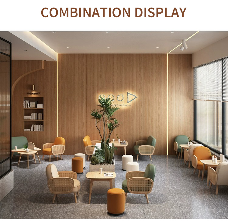 Open-layout cafe with green, orange, and beige woven armchairs paired with small wooden tables. Large windows provide ample natural light, while greenery and wooden walls add warmth to the space