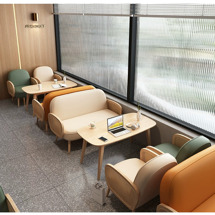 A stylish coffee shop featuring modern rattan armchairs in green, beige, and orange with matching minimalist wooden tables, bathed in natural light through textured glass windows.