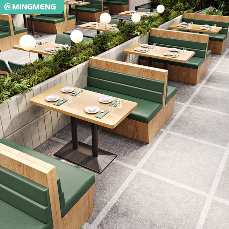 Restaurant booth seating with wooden tables and green cushions, surrounded by greenery dividers, creating a cozy and stylish dining atmosphere