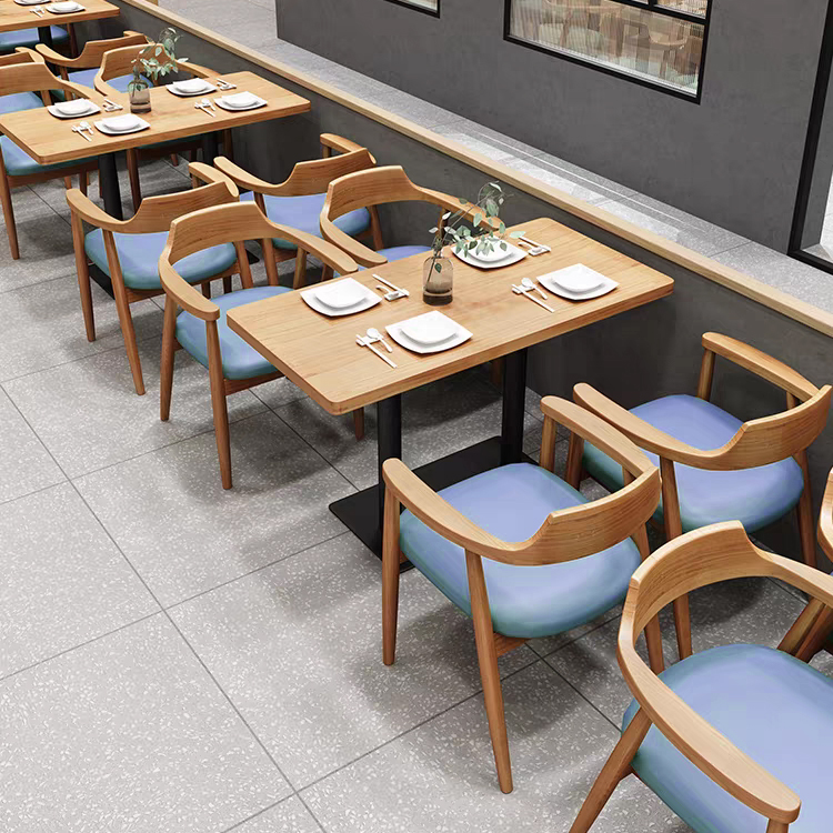 Close-up of restaurant dining tables and wooden chairs with blue padded seats, arranged for a modern dining setup.