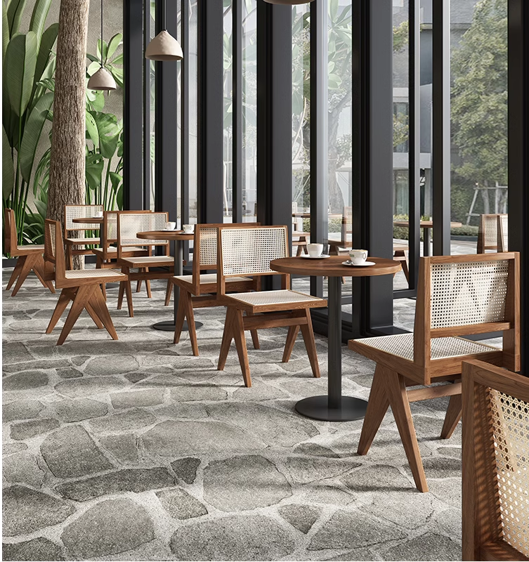 Restaurant dining area featuring rattan chairs and round wooden tables near large glass windows, creating a natural and bright ambiance.