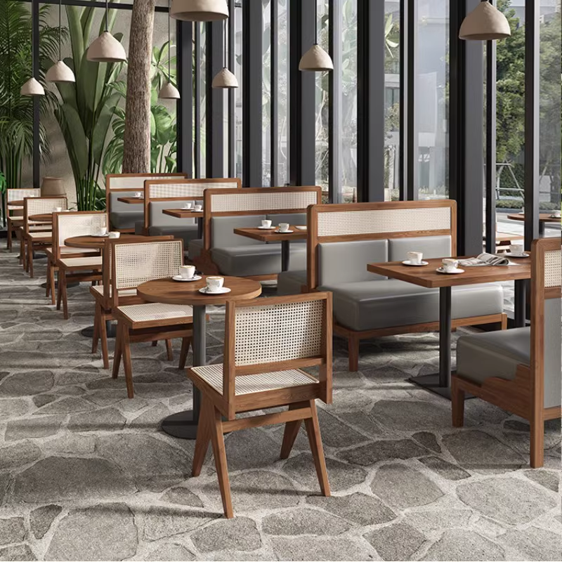 Modern restaurant interior featuring wooden rattan chairs, booth seating, and round wooden tables, surrounded by large glass windows and natural decor.