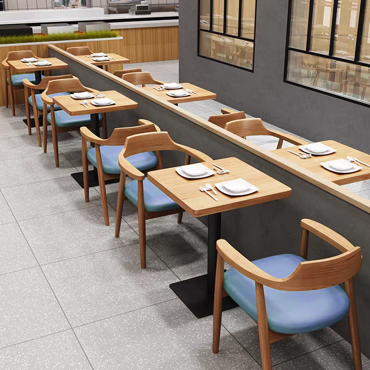  Long booth seating with modern wooden tables and matching blue padded chairs in a contemporary restaurant layout.