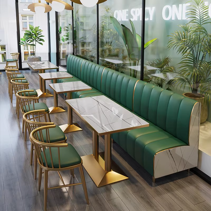 Modern booth seating with green upholstery and gold accents, paired with marble-top tables.