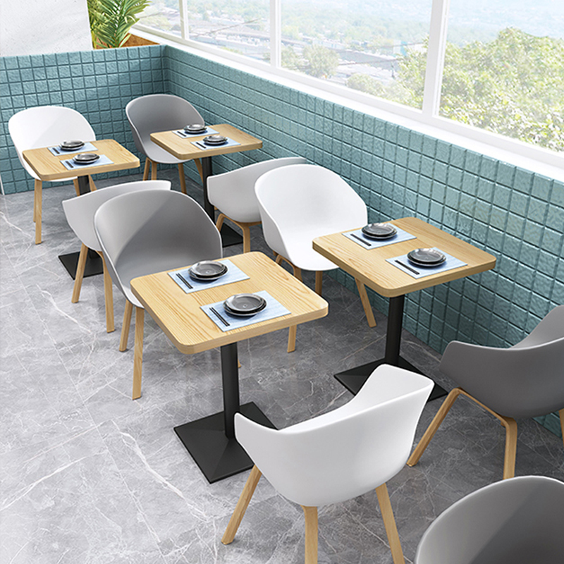 Contemporary dining area with white and grey shell chairs, wooden tables, and a bright tiled wall backdrop