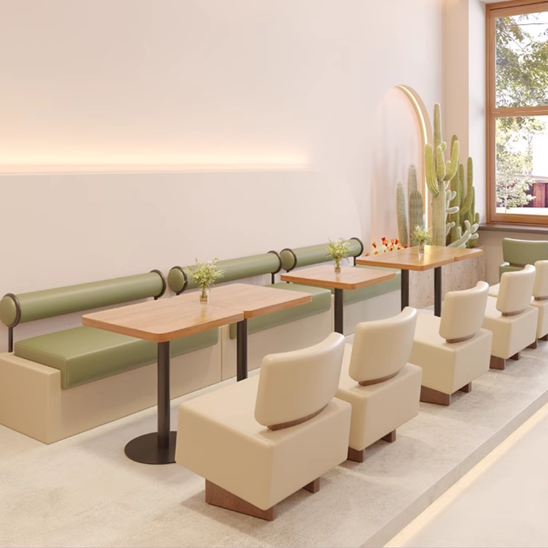 A modern round wooden table with green and beige chairs, set in a minimalist café lounge.