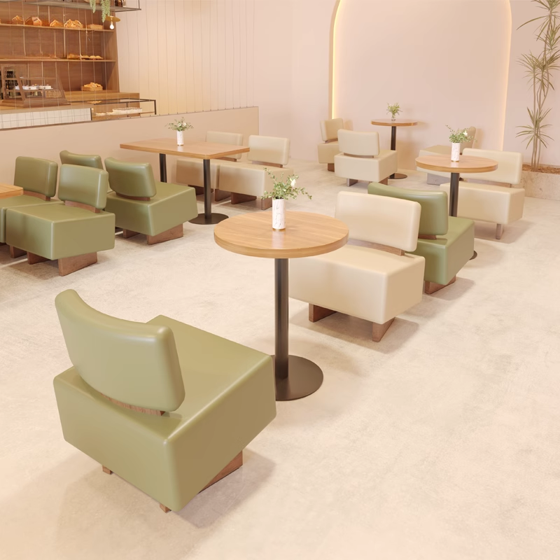 A modern café lounge featuring two-seater green and beige chairs paired with wooden tables.