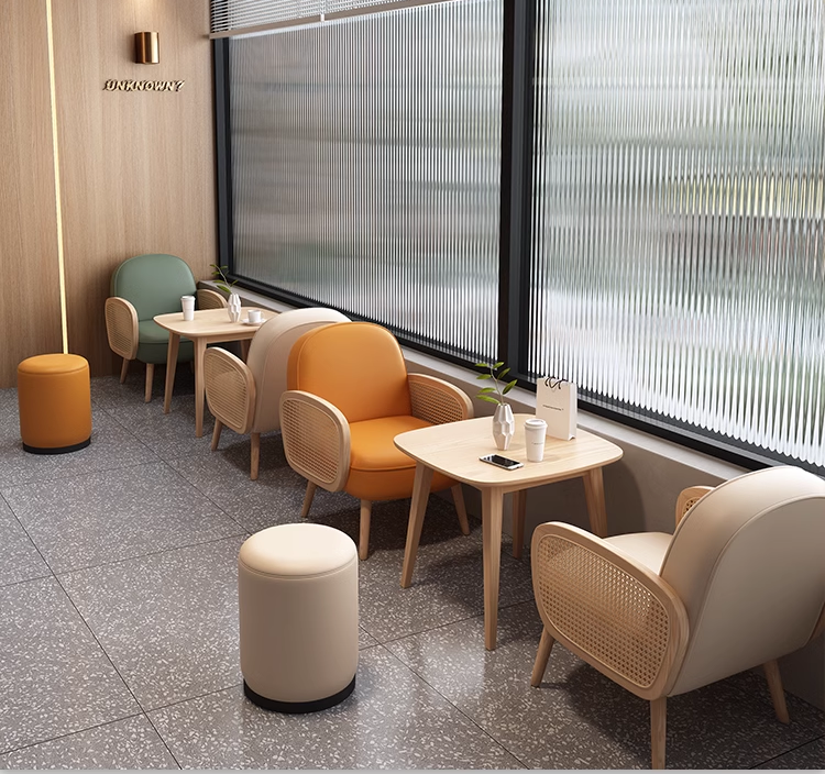 A lively coffee shop seating area featuring colorful chairs in green, orange, and neutral tones with small tables and a peaceful view outside.