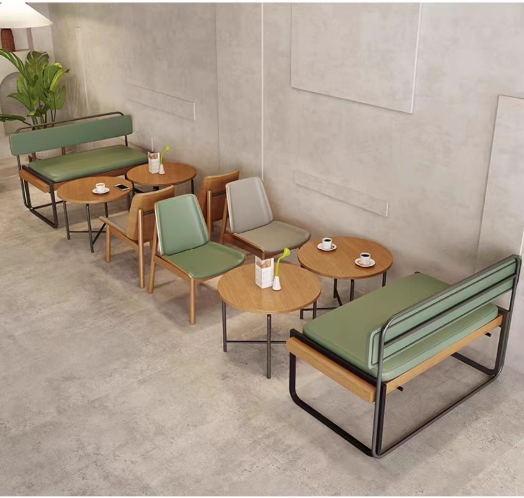 Cozy cafe interior showcasing green benches, round wooden tables, and minimalist chairs, arranged against a neutral concrete wall for a modern aesthetic.