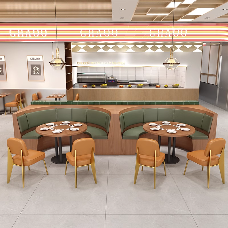 Restaurant interior with curved booth seating, green cushions, round wooden tables, and an open kitchen in the background.