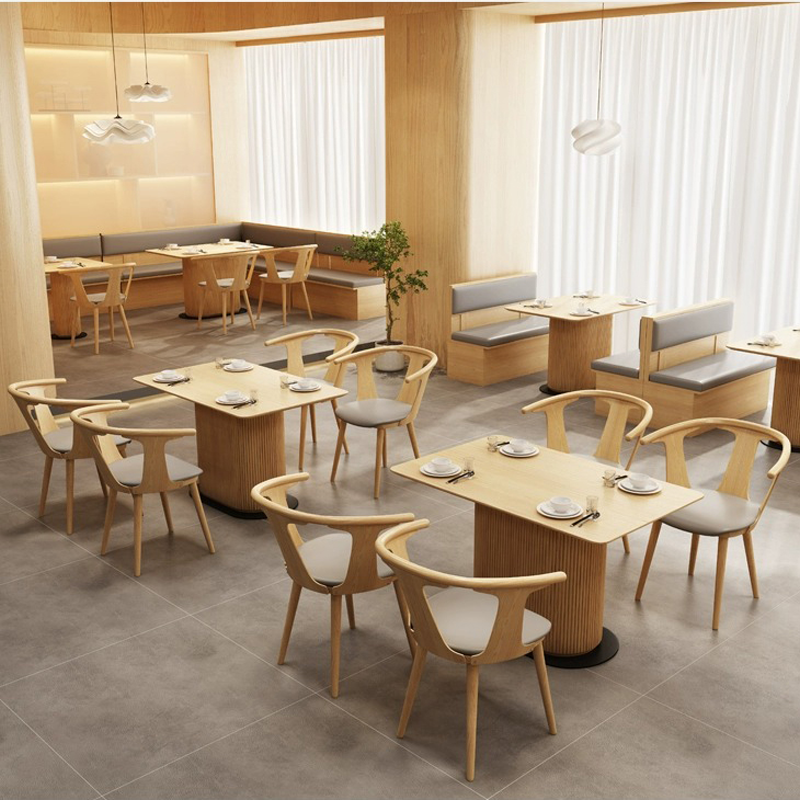 Restaurant interior showcasing light wooden booths and chairs with gray cushions, arranged around rectangular tables in a minimalist design.