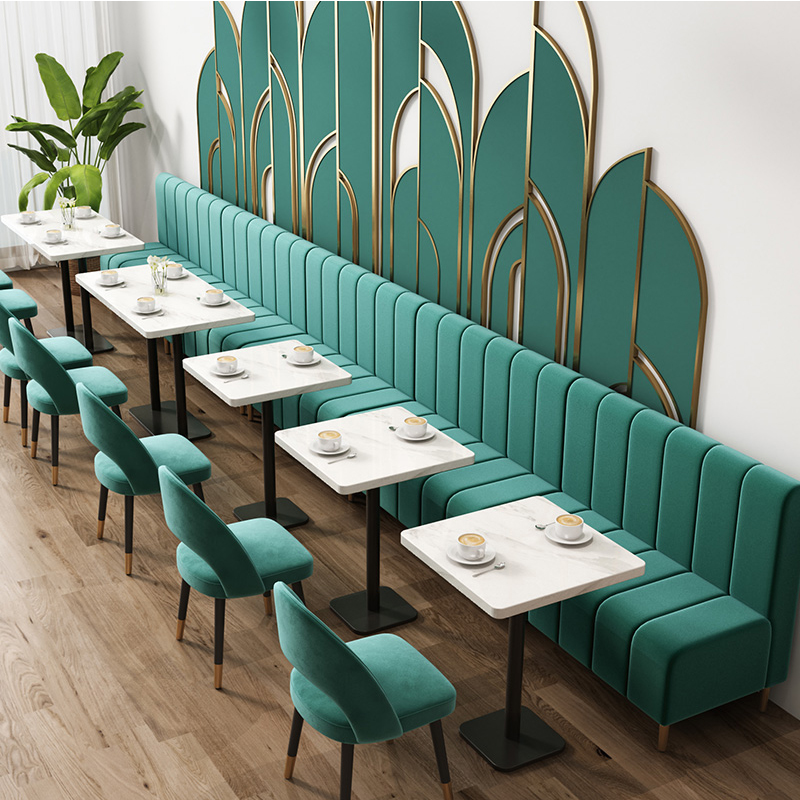 Elegant green restaurant booth seating with matching modern chairs and marble-top tables, set in a stylish dining area.