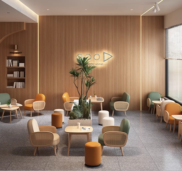 A modern lounge area featuring various colorful chairs in orange, green, and white, along with small tables and plants. The wood paneling on the walls adds warmth to the space.