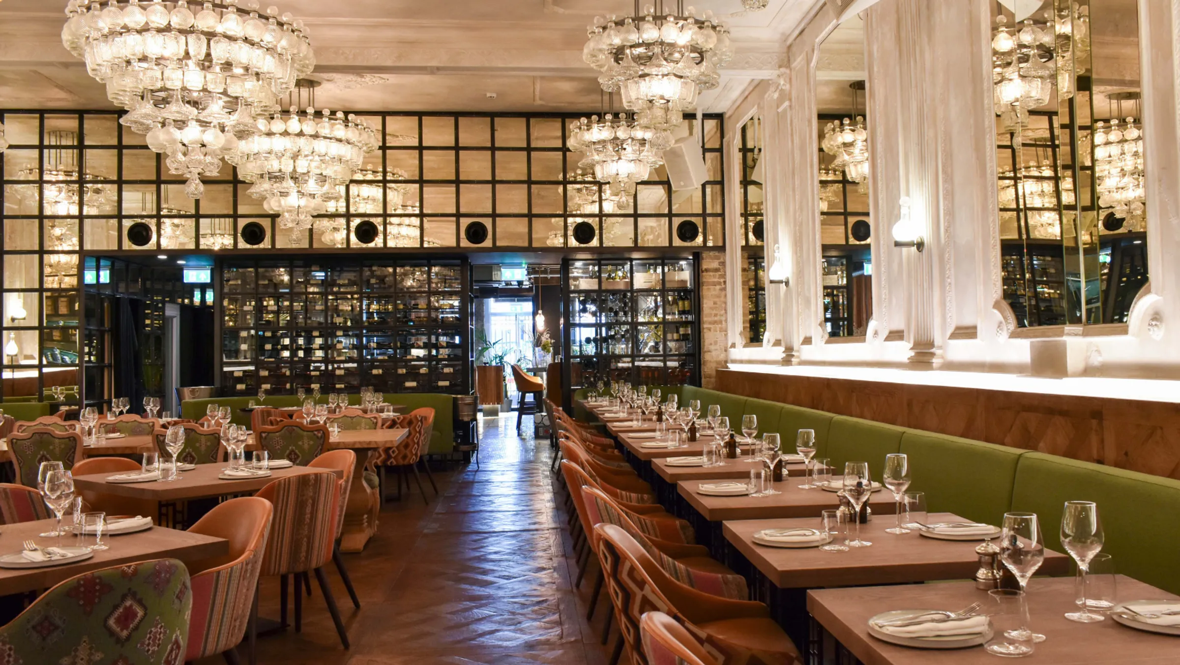 Elegant dining space with luxurious chandeliers, green upholstered seating, and mirrored walls.