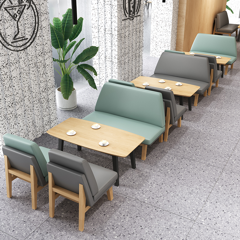 Modern cafe seating arrangement with green and gray cushioned benches and chairs paired with light wooden tables, set in a stylish dining area.