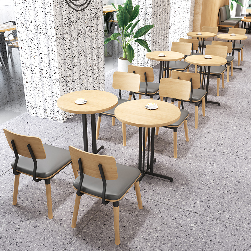 Modern cafe seating arrangement with round wooden tables and light wood chairs featuring gray cushions and black metal frames.