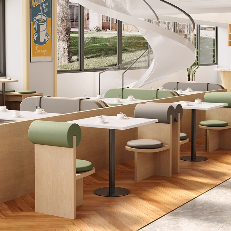 Modern café seating with green cushioned chairs, white tables, and a spiral staircase, perfect for stylish dining spaces