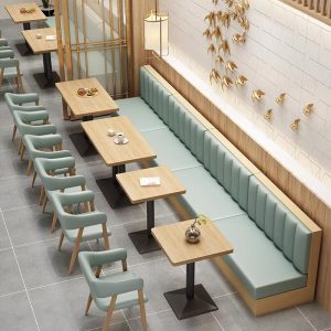 Modern cafe seating arrangement featuring wooden dining tables, upholstered booth seating in mint green, and matching chairs with curved backrests.