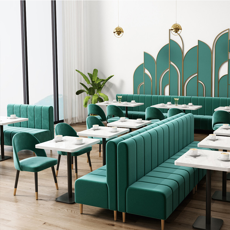 Modern green restaurant booths paired with sleek marble tables and elegant velvet chairs in a contemporary dining space.