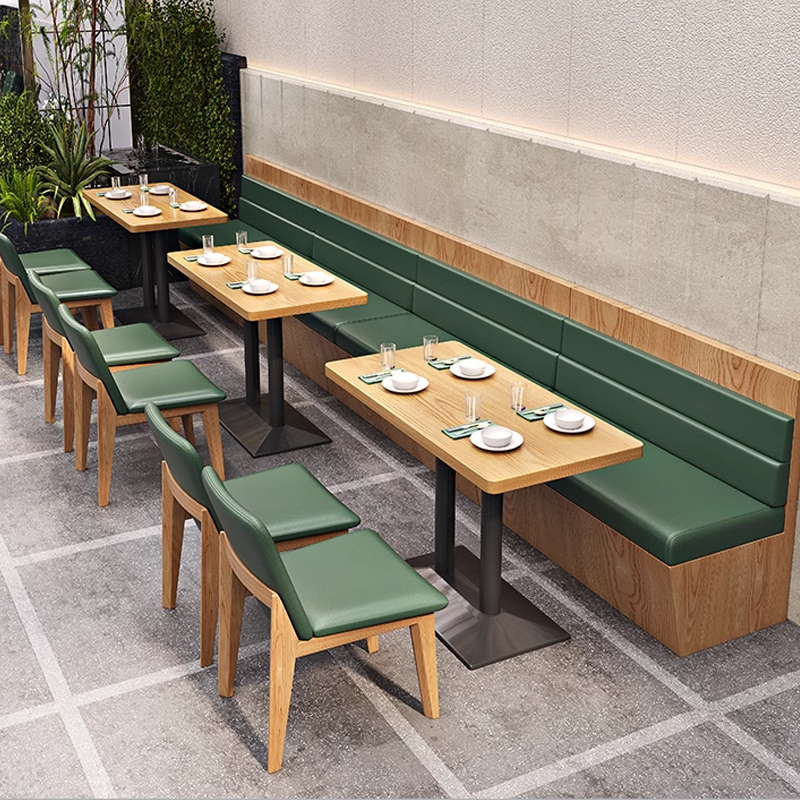 Modern outdoor restaurant seating with green leather chairs and booths, offering a cozy and contemporary dining environment.