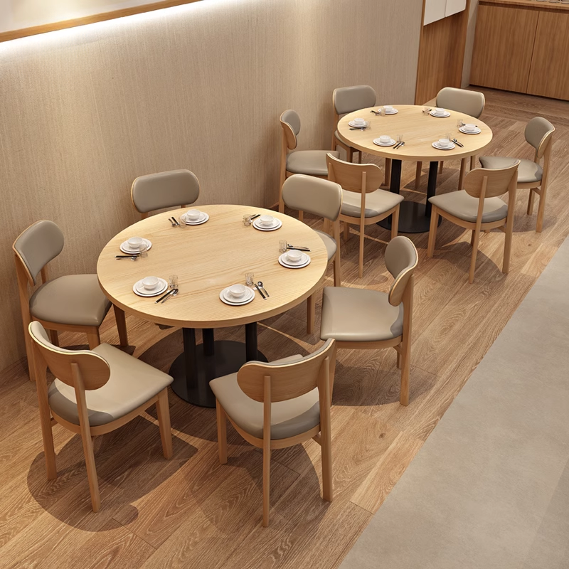 Dining area table and chairs arrangement in a modern restaurant with light wooden tables and beige cushioned chairs.