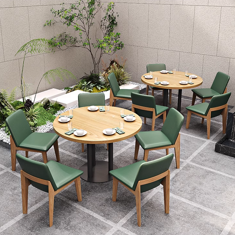 Outdoor garden dining area with round wooden tables and green leather chairs in a modern restaurant, surrounded by lush plants and greenery.