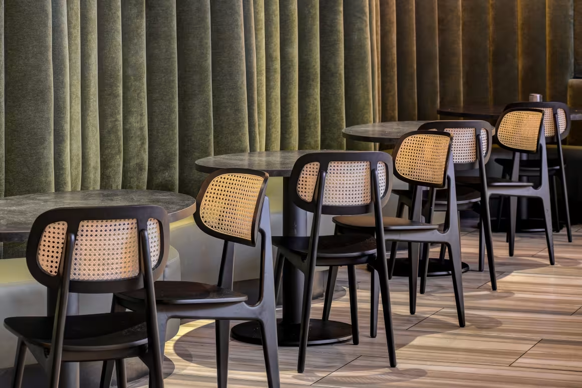 Modern rattan-back chairs with black frames in a stylish dining area featuring dark velvet curtains and stone tables.