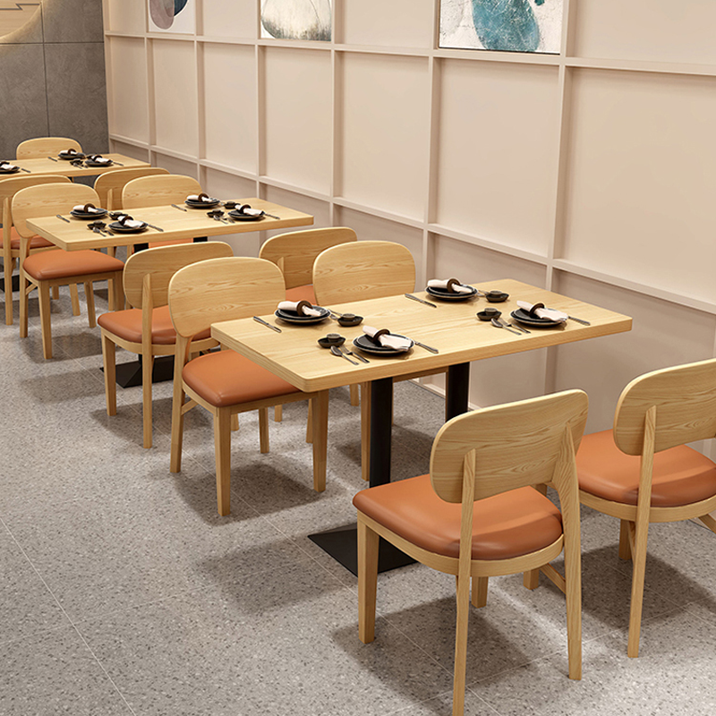 Restaurant dining area with wooden chairs featuring orange cushions and rectangular dining tables