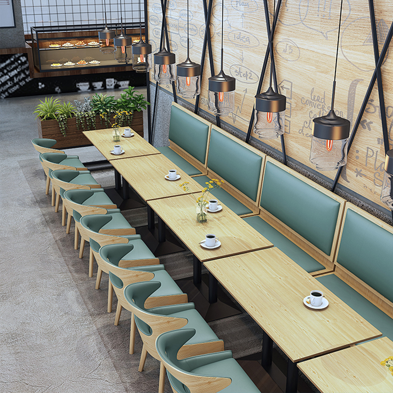 Cozy restaurant booths with green cushions, wooden tables, and industrial-style lighting, perfect for an inviting dining atmosphere.