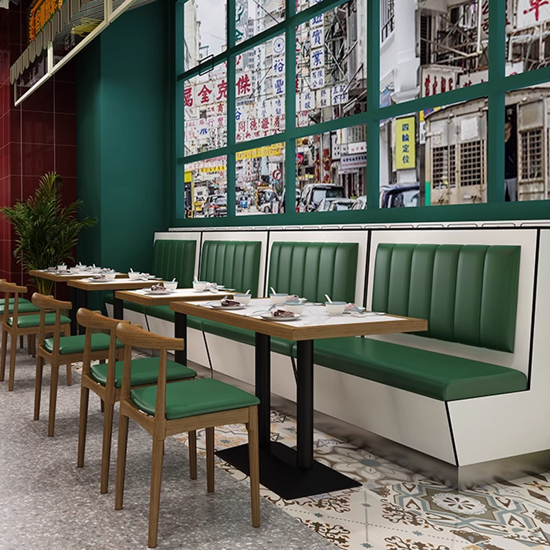 Restaurant dining area featuring green booth seating, wooden tables, and an urban view through large windows, offering a vibrant and welcoming ambiance.