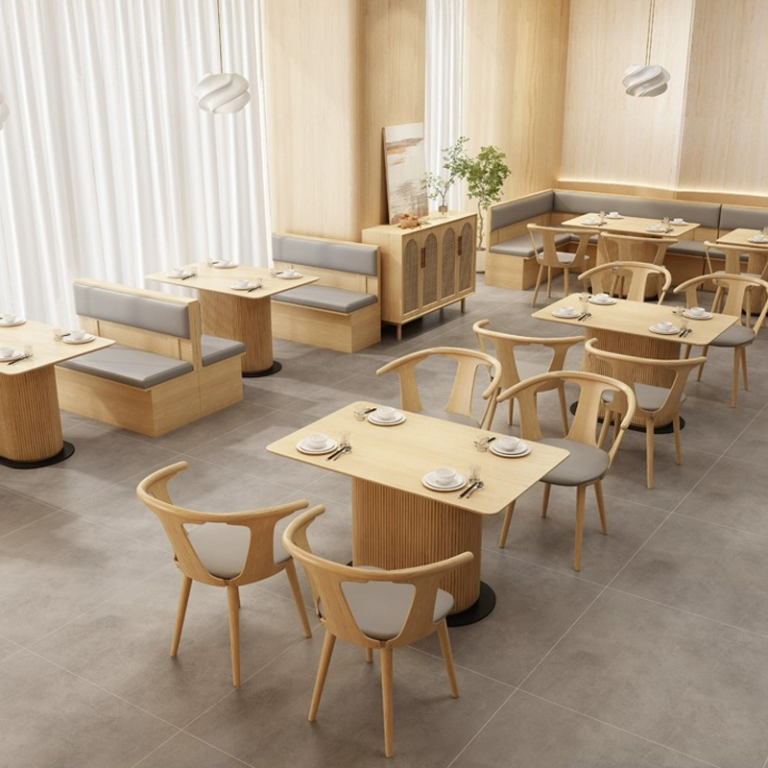 Restaurant interior showcasing light wooden booths and chairs with gray cushions, arranged around rectangular tables in a minimalist design.