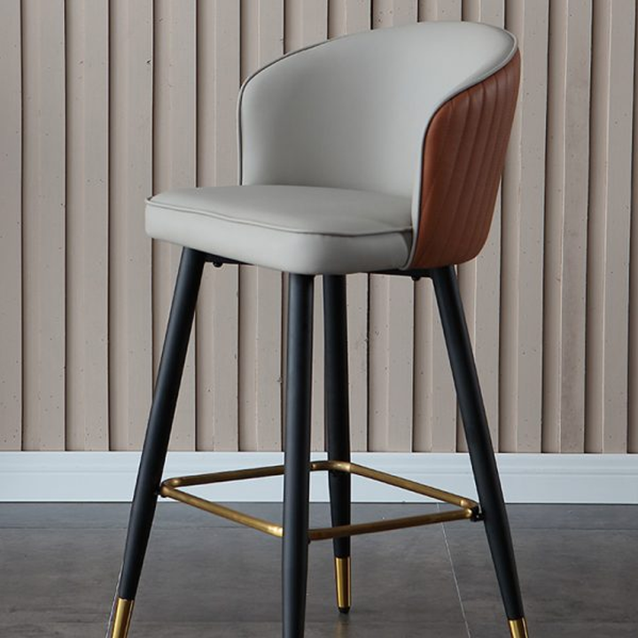 Modern bar stool with black metal legs, orange and gray PU leather seat and backrest with golden footrest, suitable for contemporary interiors.