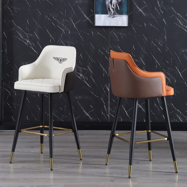 Two brown and white barstools with tufted leather seating and backrests, supported by black metal legs with golden tips.