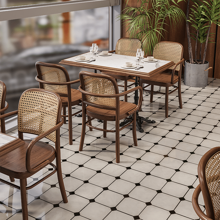 Modern restaurant dining area featuring wooden cane-back chairs, marble tables, and tiled floor with plants in the background.