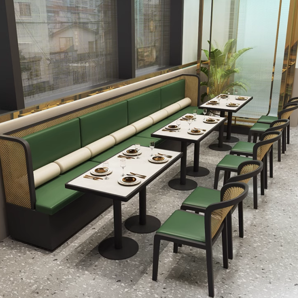 Elegant dining area featuring green-cushioned booths and chairs with cane backs, marble tables set for dining.