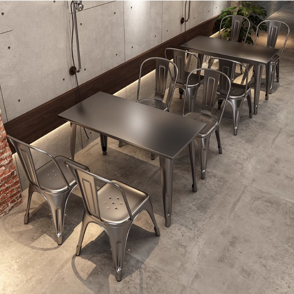 Industrial metal dining tables paired with matching chairs in a modern setting, featuring polished surfaces and concrete flooring.