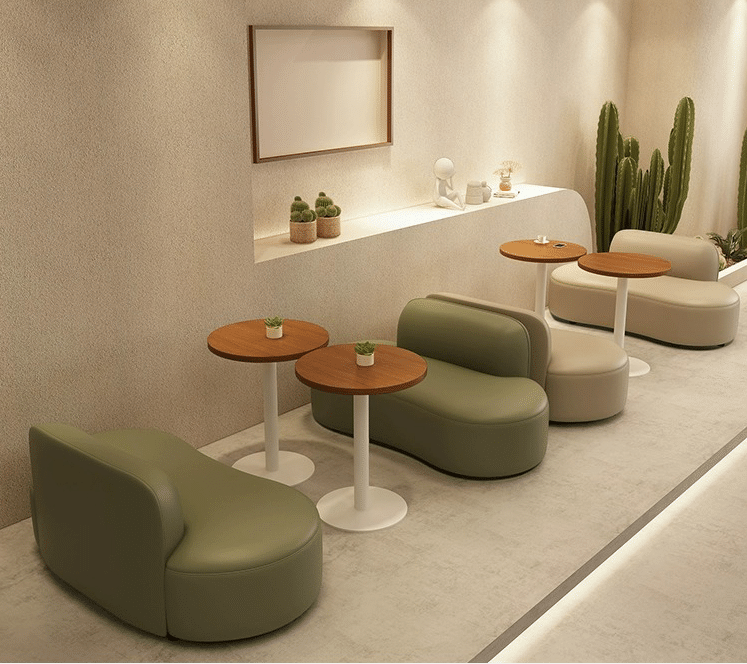 Minimalist café with green and white lounge chairs, wooden round tables, and soft lighting, featuring decorative plants and art pieces on the walls.