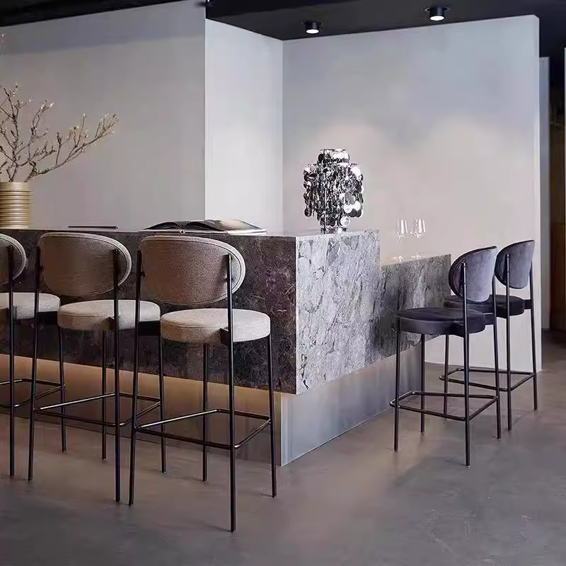 Stylish modern bar stools with black metal frames and soft, padded seats in different colors, arranged around a minimalist bar.