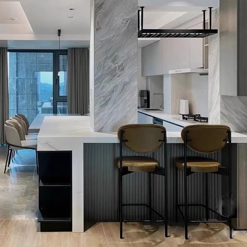 Modern bar stools with brown upholstered seats and black frames, placed at a kitchen bar with a marble countertop.