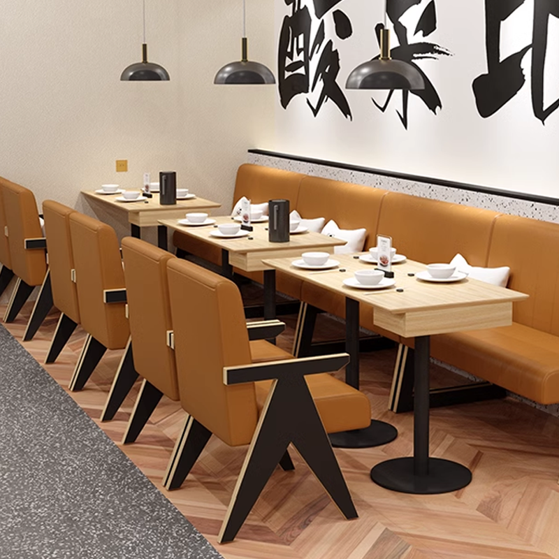 Restaurant booth seating with cushioned tan chairs, wooden tables, and modern industrial lighting fixtures.