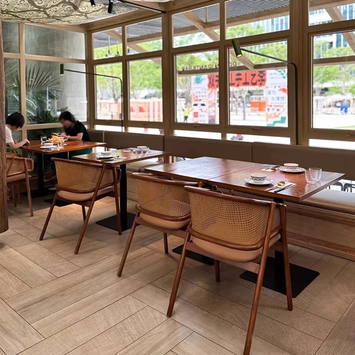 Restaurant interior featuring modern cane back chairs and a wooden dining table design, with large windows allowing natural light.